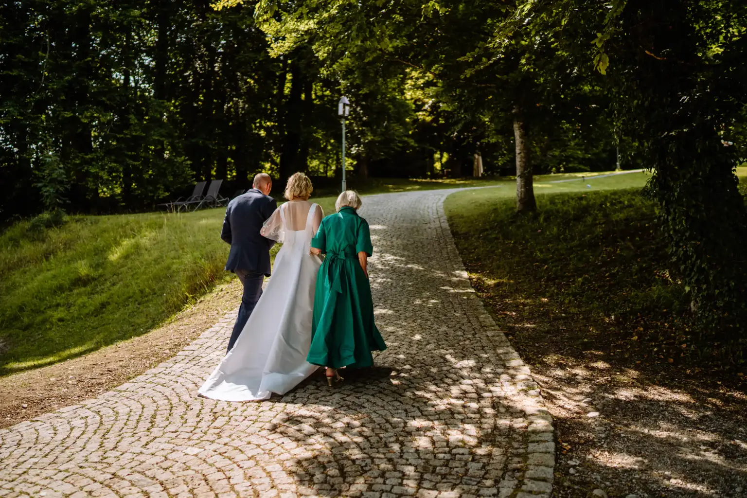 Braut und Bräutigam gehen gemeinsam mit der Brautmutter zur Trauung am See