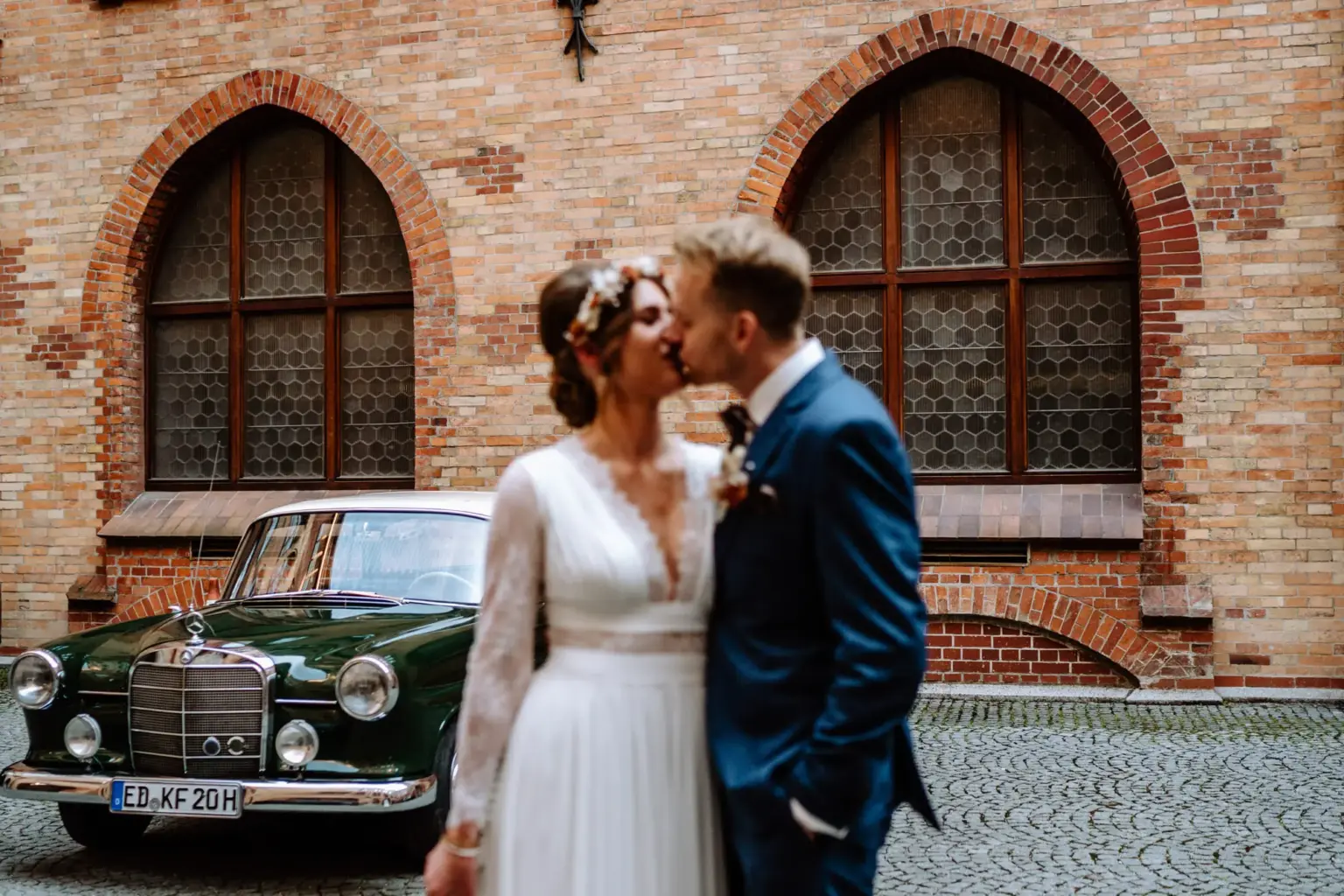 Braut küsst Bräutigam im Hof vom Rathaus München vor ihrem Hochzeitsauto