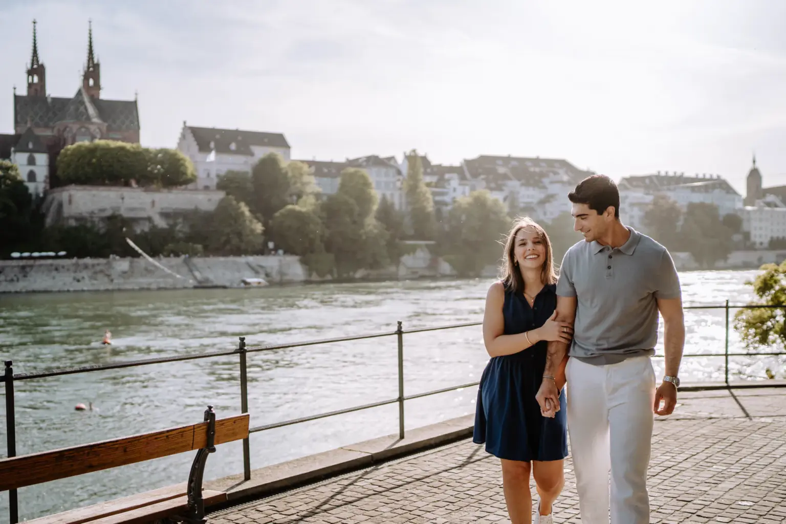 Paar geht Hand in Hand am Rhein entlang mit dem Basler Münster im Hintergrund