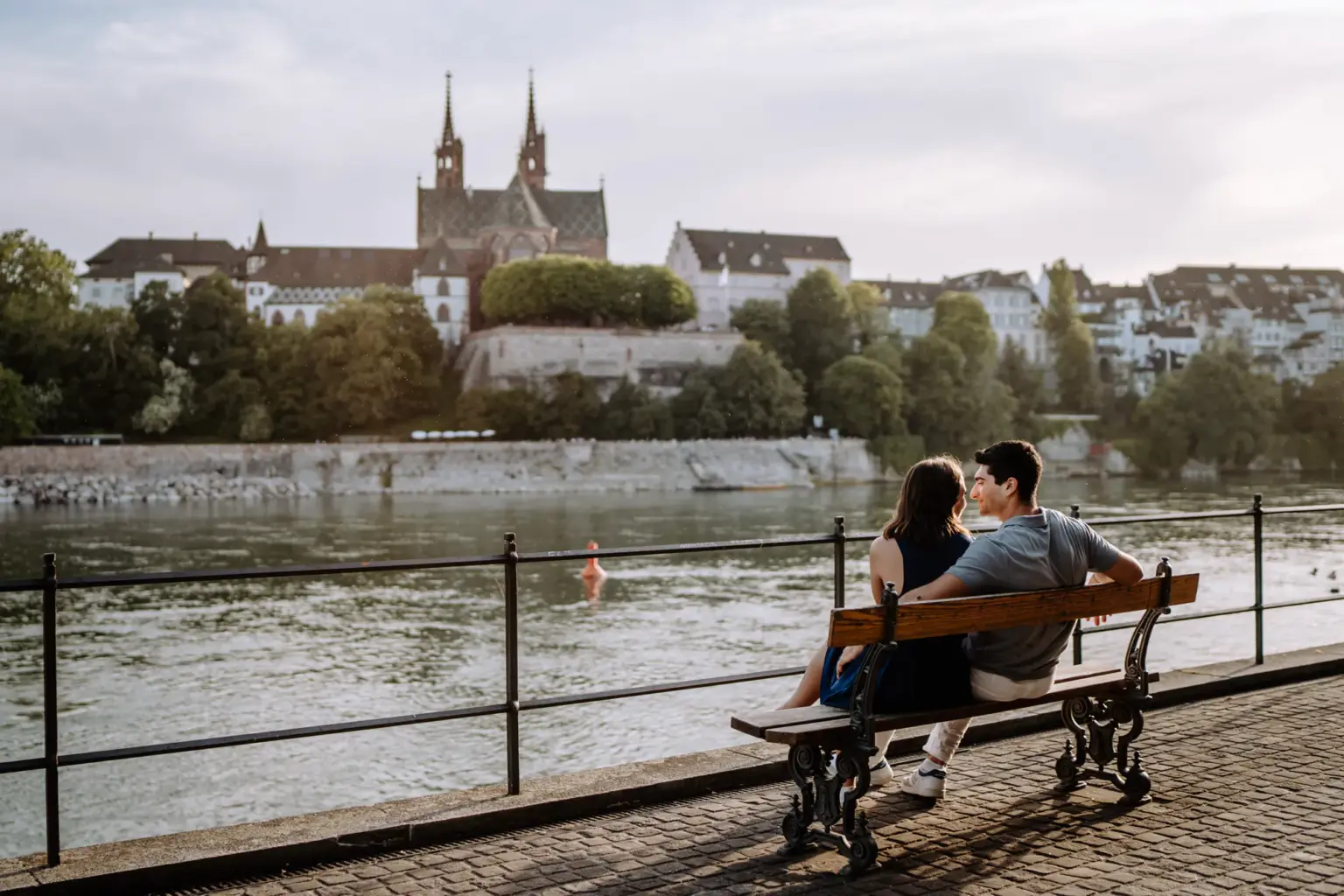 Paar sitzt auf einer Bank am Rhein mit Blick auf das Basler Münster